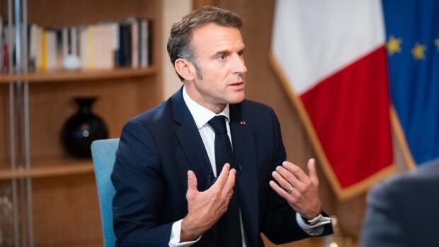 France’s President Emmanuel Macron sits in a chair wearing a blue suit as he is interviewed by CBC’s Chief Political Correspondent Rosemary Barton and Radio-Canada's Parliamentary Bureau Chief Louis Blouin who are off camera.