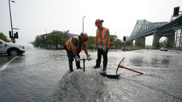 Two men in consturction gear work in a flooded street.