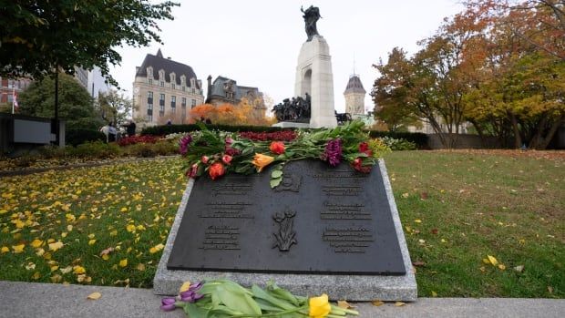 Flowers lay on a plaque on a lawn in front of a larger memorial.