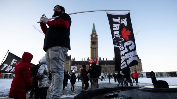 A person supporting a cross-country convoy protesting measures taken by authorities to curb the spread of COVID-19 holds a flag with an expletive targeting Prime Minister Justin Trudeau in front of Parliament Hill as truckers arrive in Ottawa on Friday, Jan. 28, 2022.