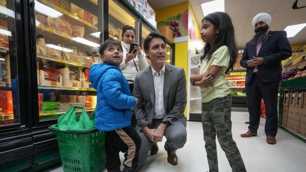 A man in a grey suit crouches down to speak to two children in a grocery store aisle.