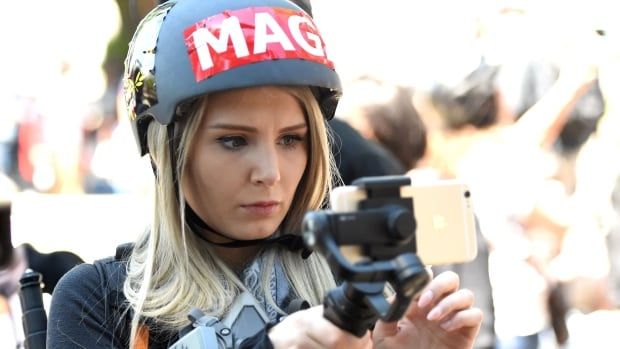 A woman in a MAGA helmet live streams with her iPhone at a rally.