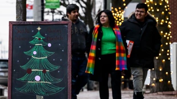 Several people walk near a sandwich board with a Christmas tree doodle.