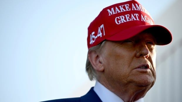 A man in a suit wears a red Make America Great Again hat. 