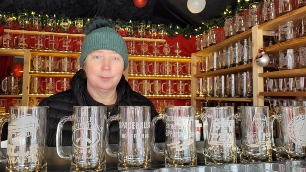 A woman stands in a Christmas market stall with sand-blasted glass mugs around her.