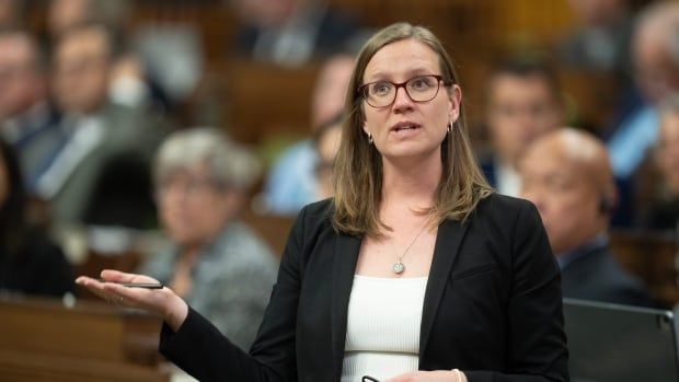 A woman in a black blazer and white shirt gestures with her hand as she speaks in the House of Commons.