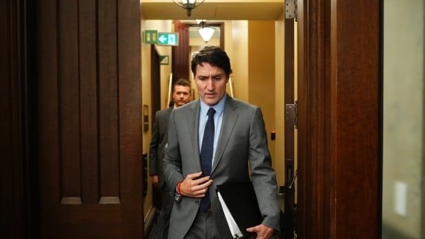 A politician in a grey suit walks through large wooden doors with cameras pointed at him.