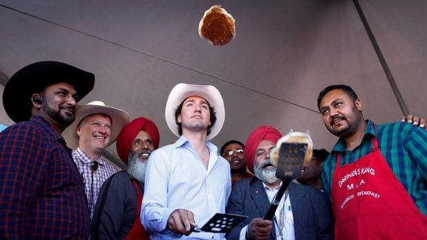 Liberal Leader Justin Trudeau, centre, flips pancakes at a Stampede breakfast, with supporters watching him.