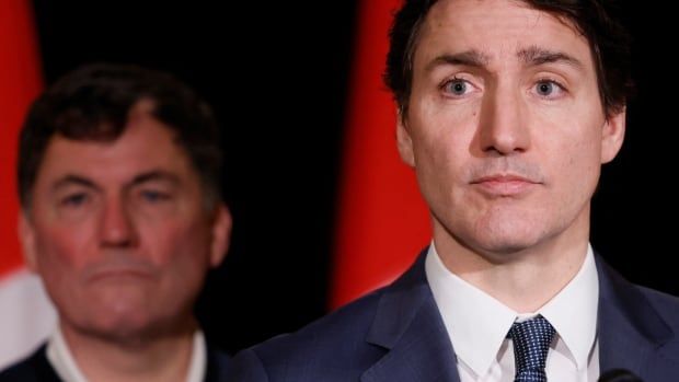 Two men seen in front of a Canadian flag.