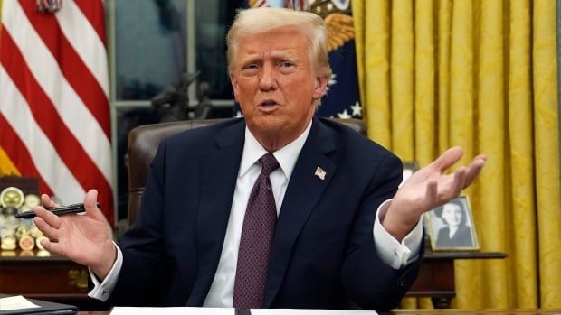 President Donald Trump sits behind his desk and talks to reporters as he signs executive orders in the Oval Office of the White House.