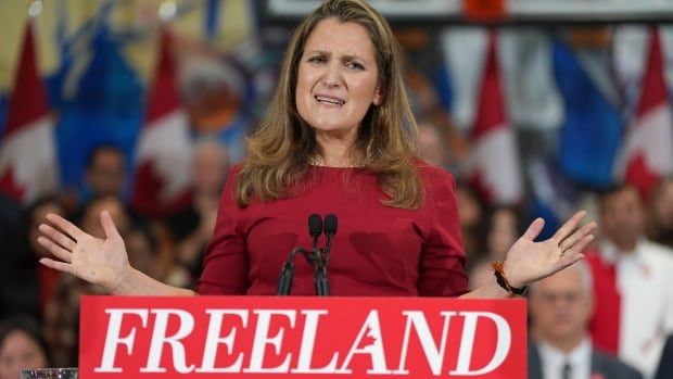 Chrystia Freeland speaks into a microphone at a podium. Behind her are supporters of her campaign.