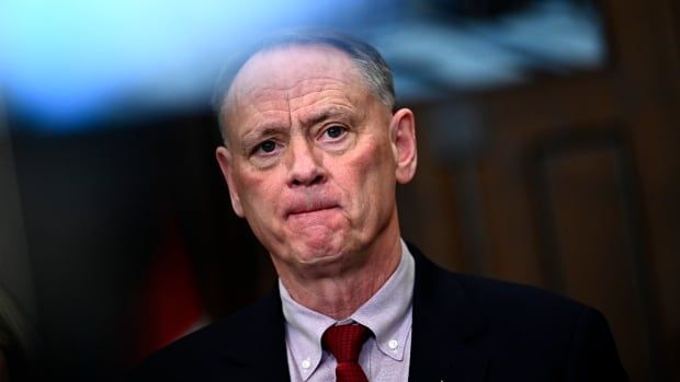 A man in a suit listens to a question during a news conference.