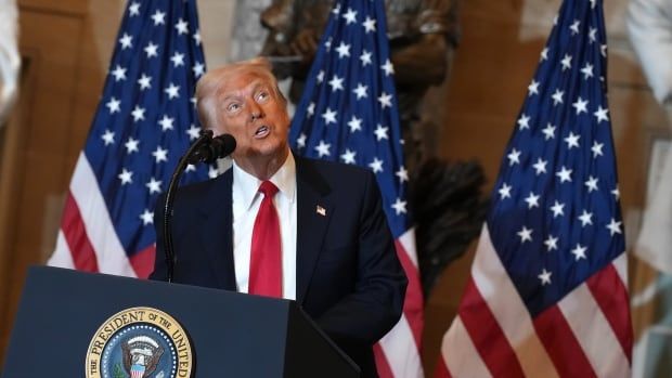 A man in a suit looks upward while standing at a podium that bears a crest reading 'Seal of the President of the United States.' Three flags are seen behind him.