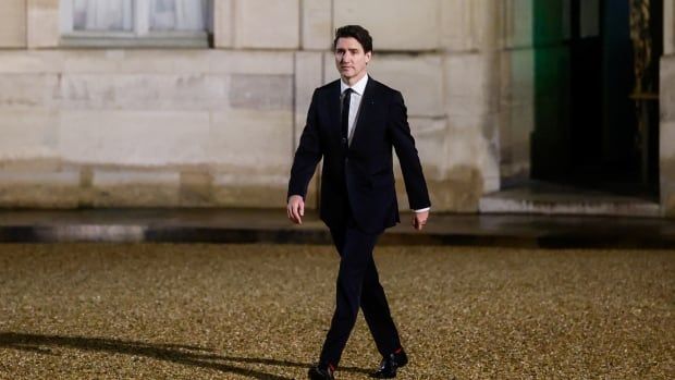 A man in a dark suit walks alone outside a building.