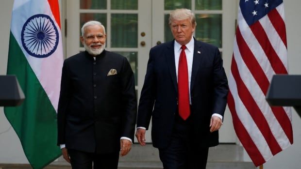 Two men walk outdoors with Indian and United States flags around them.