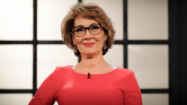 A woman in a coral shirt wearing red lipstick looks past the camera. 