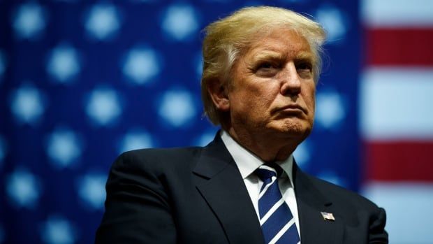 Donald Trump profile shot at a rally behind a large U.S. flag