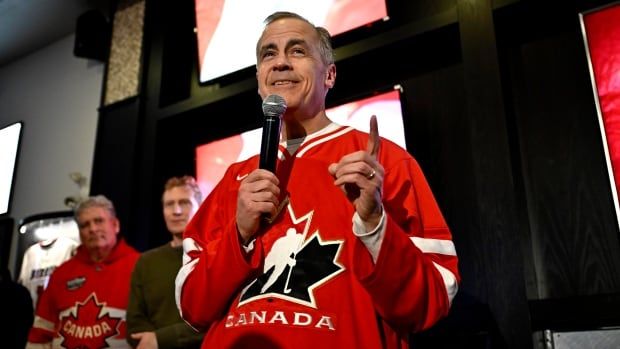 A man holds a microphone while wearing a Team Canada hockey jersey.