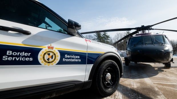 A black helicopter parked next to a border service vehicle on a winter day.