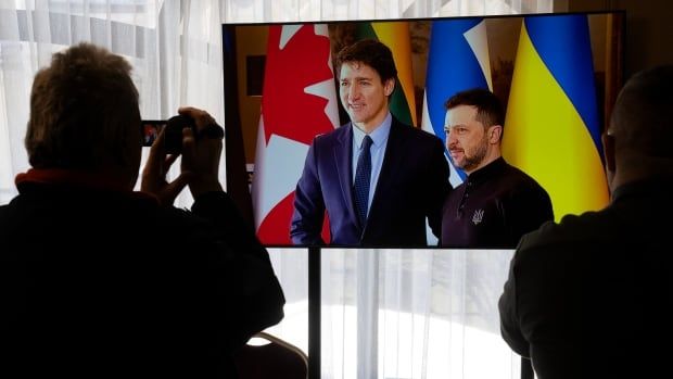 Journalists film a television screen as Ukrainian President Volodymyr Zelenskyy greets Canadian Prime Minister Justin Trudeau in Kyiv, Ukraine.