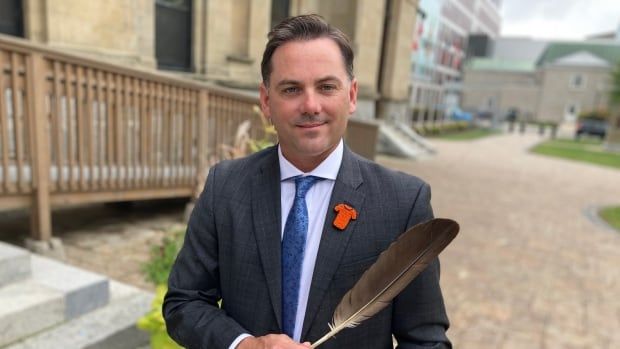 Man stands holding a feather in front of the Legislature in Fredericton