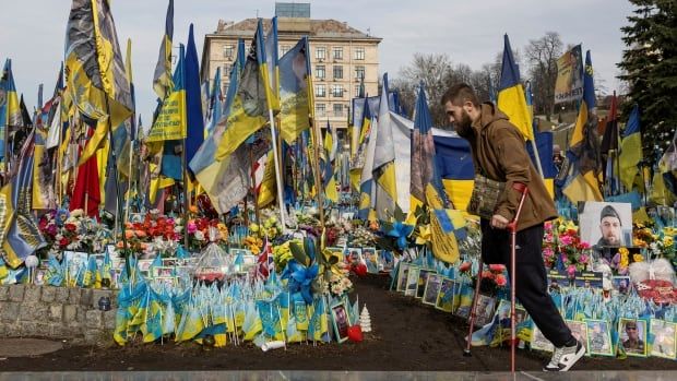 A man in crutches walks in front of ukrainian flags.