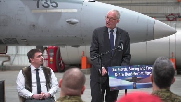 A man speaking at a podium inside an aircraft hangar.