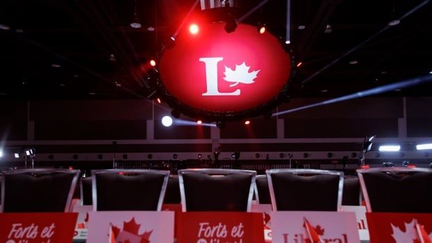 Red-and-white signs are seen on reserved chairs at an event centre. A large sign overhead has a letter "L" and a maple leaf.