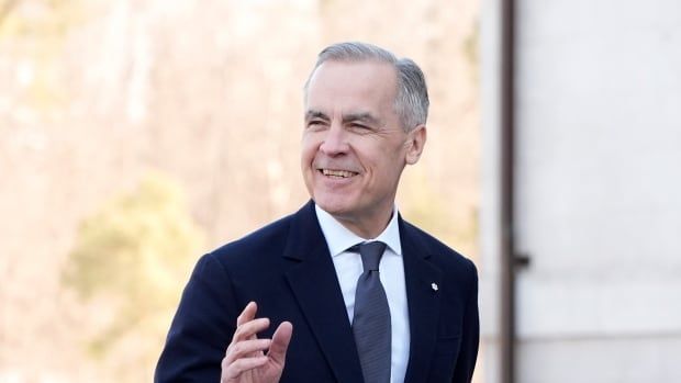 A grey-haired man in a suit and tie walks into a stone building. 