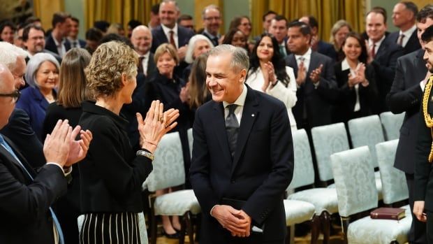 A man in a suit smiles as a crowd claps for him.