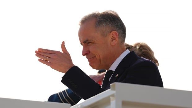 Prime Minister Mark Carney gestures as he steps off the plane in Stansted, England,