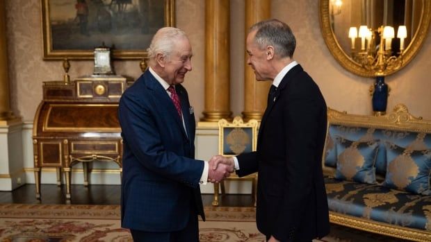 King Charles III shakes hands with Prime Minister Mark Carney at Buckingham Palace in London. The pair are indoors. 