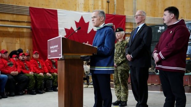 A man stands and speaks at a podium as others look on.