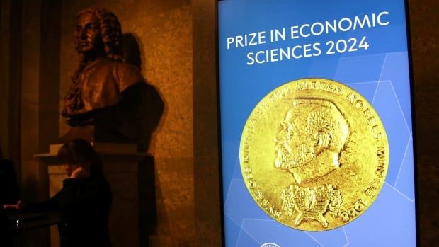 A screen next to a bust shows a Nobel medal and the words "PRIZE IN ECONOMIC SCIENCES 2024"