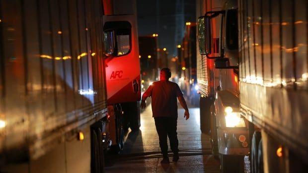 A man walks between a line of trucks on a road at night