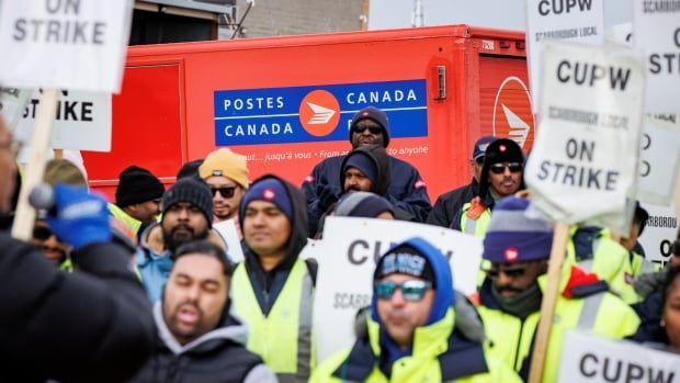 Picketers hold signs reading "CUPW on strike" with a Canada Post Truck in the background