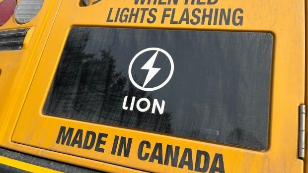 A Lion Electric logo is placed on a window on the back of a yellow school bus. 