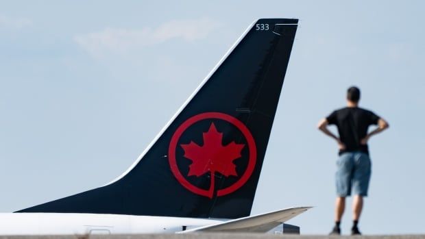 A blurry man stands in the foreground at the right side of the image. The in-focus plane tail beyond him shows the red Air Canada symbol. 