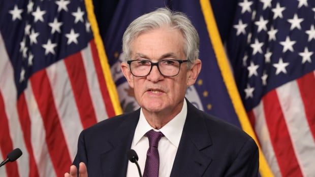 A man wearing glasses stands at a podium with an American flag on display behind him.