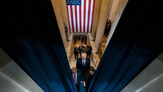 An elevated view shows a man in a suit entering a room through a large long velvet curtain.