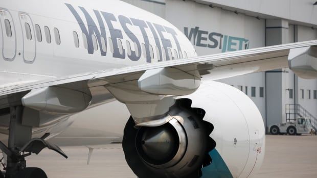 The wing and front portion of a passenger plane with the name 'WestJet' is seen outside of a hangar.