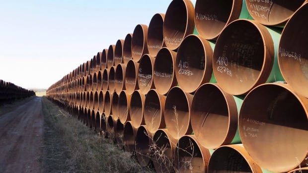 Cylindrical pipes are shown in a photo along a plain of grass.