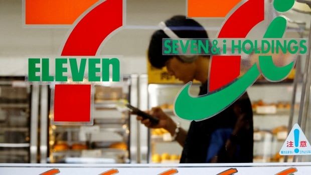 A person is seen unfocused through the window of a 7-Eleven. 