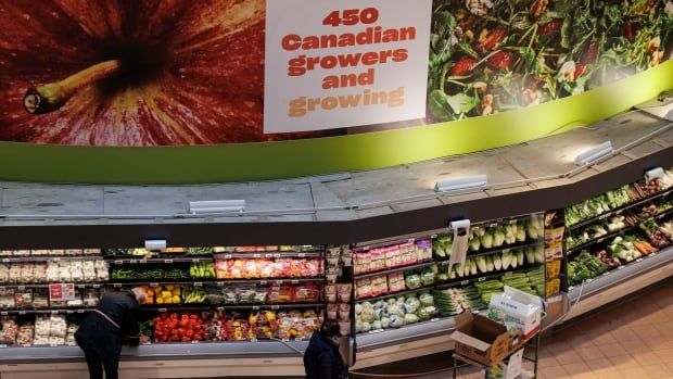 Shoppers wander around a grocery store, where a sign above the produce section reads, '450 Canadian Growers and Growing.'