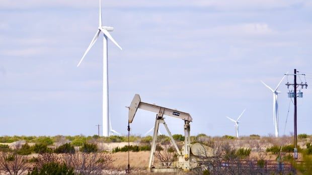 A white wind turbine towers above a beige oil pumpjack.