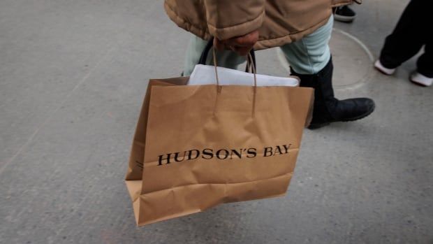 A person carries a paper brown shopping bag printed with the words Hudson's Bay.