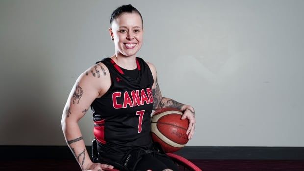 A female wheelchair basketball player is seen wearing a Canadian jersey and holding a ball as she smiles for a picture.