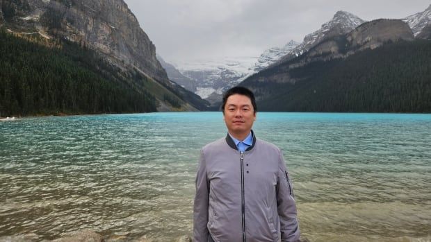 A man stands in front of an alpine lake.