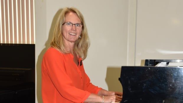 A woman wearing a red blouse seated at a piano. 