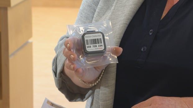 A woman holding a small square plastic device with a barcode on it, wrapped in plastic